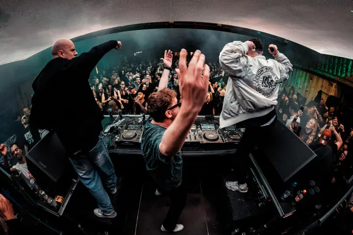Drei Acts tanzen am DJ-Pult vor der Menge